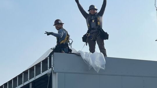 Two Crown employees celebrating while working from the roof of an enclosure