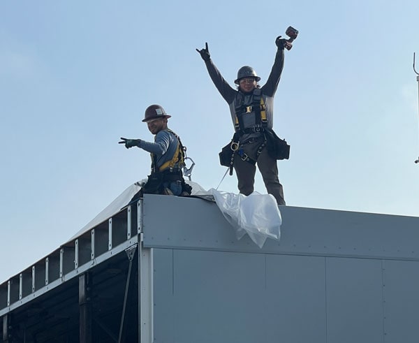 Two Crown employees celebrating while working from the roof of an enclosure